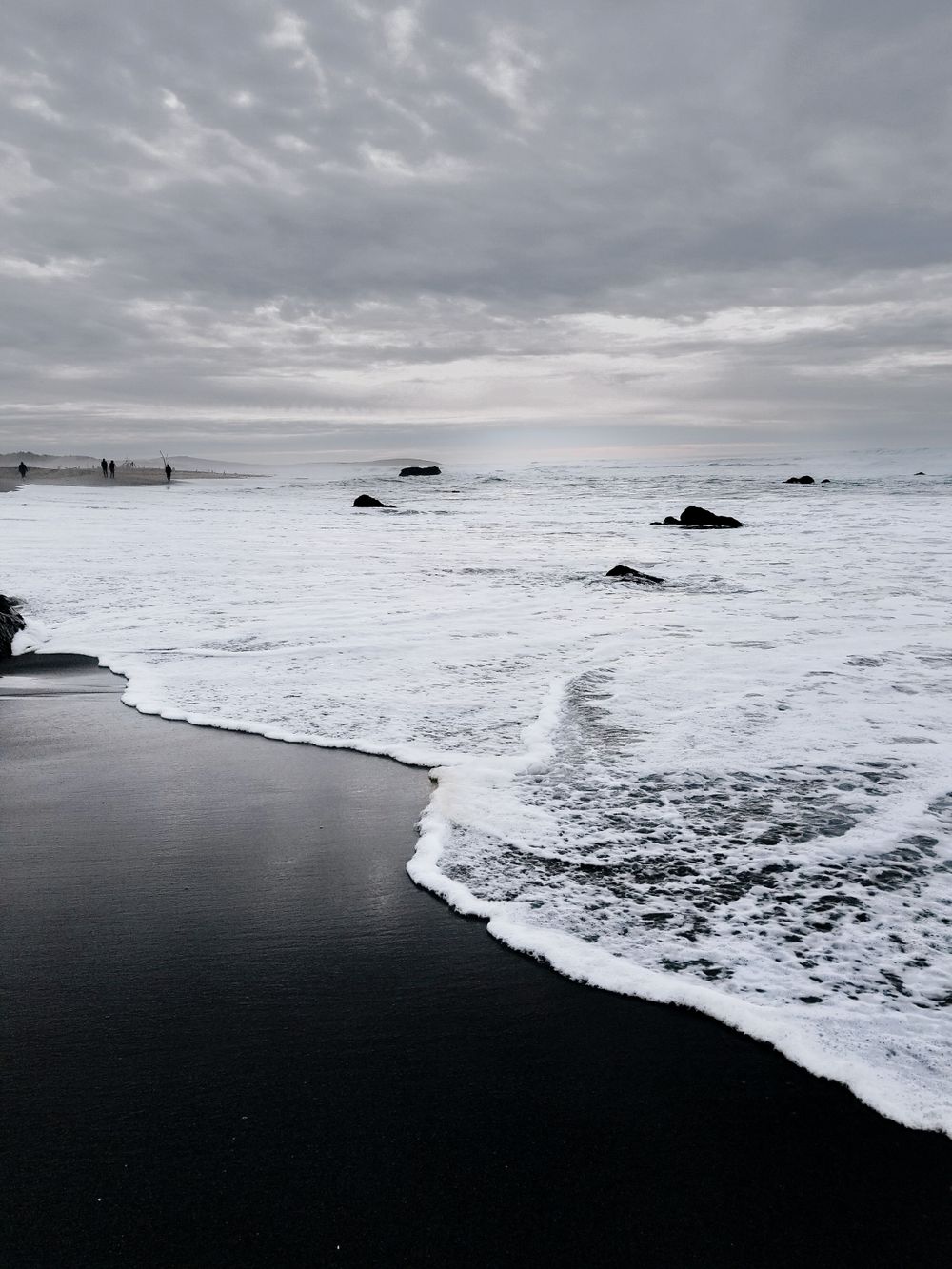 Dramatic black sand beach with white waves under cloudy sky.