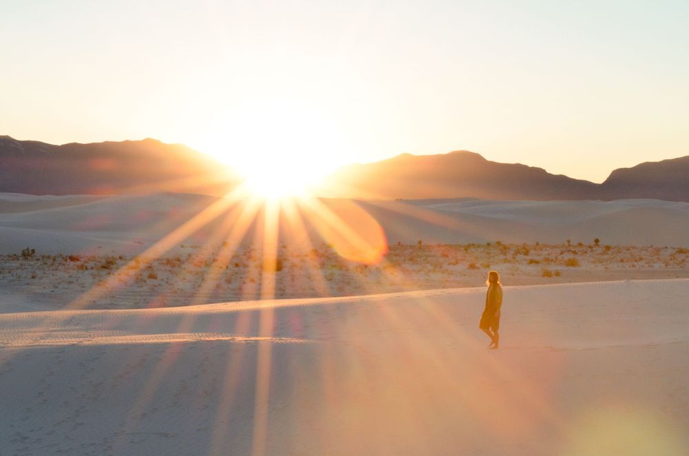 Dramatic sunset over sand dunes with sunburst rays stretching across desert landscape.