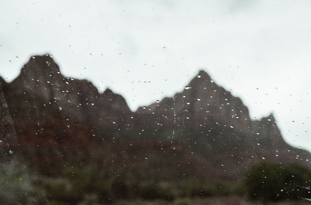 Mountain peaks silhouetted against a rainy sky with water drops on glass.