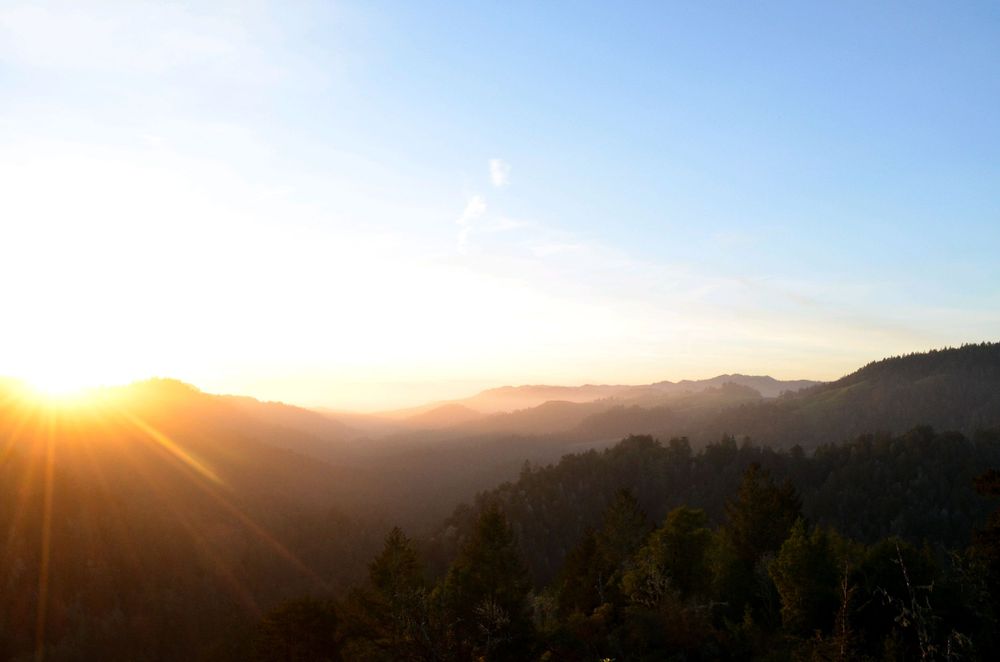 Golden sunset over misty mountain ridges with sunburst through clouds.