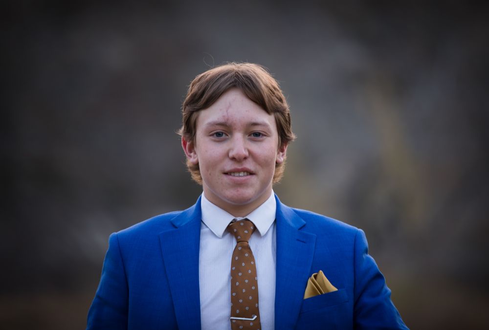 A portrait of someone wearing a bright blue suit with brown tie and yellow pocket square.