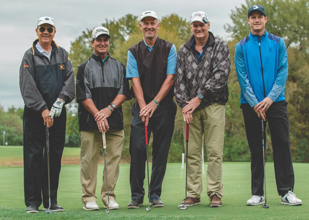 Group of golfers lined up on a green course preparing to putt.