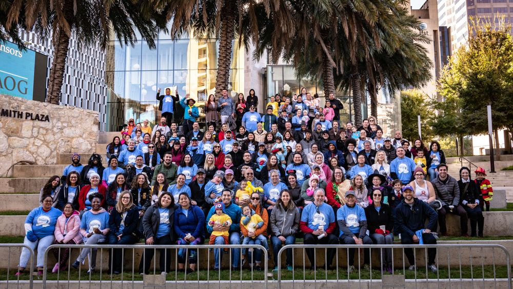 Large crowd of people gathered outdoors for a group photo with palm trees in the background.