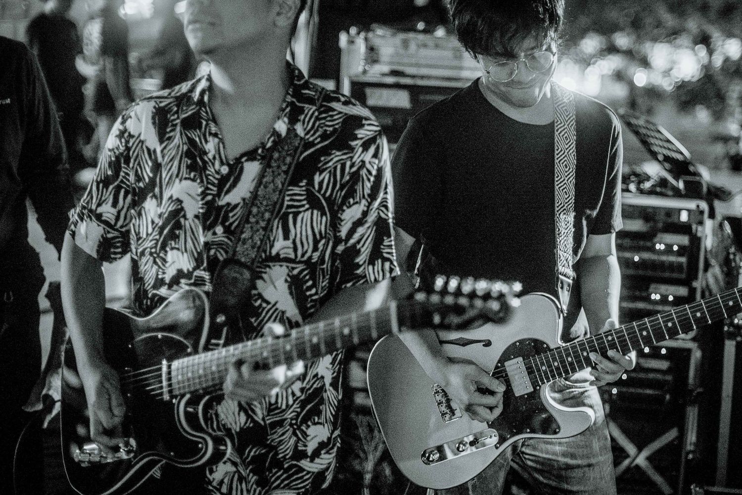 Black and white shot of guitarists performing on stage with dramatic lighting.