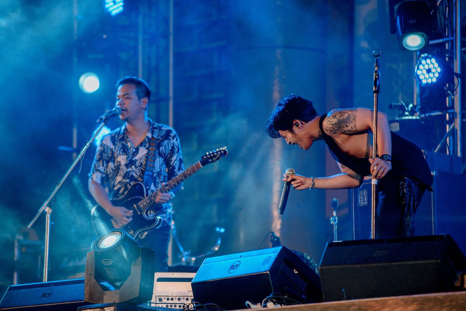 Band members perform energetically on stage with blue lighting and atmospheric effects.