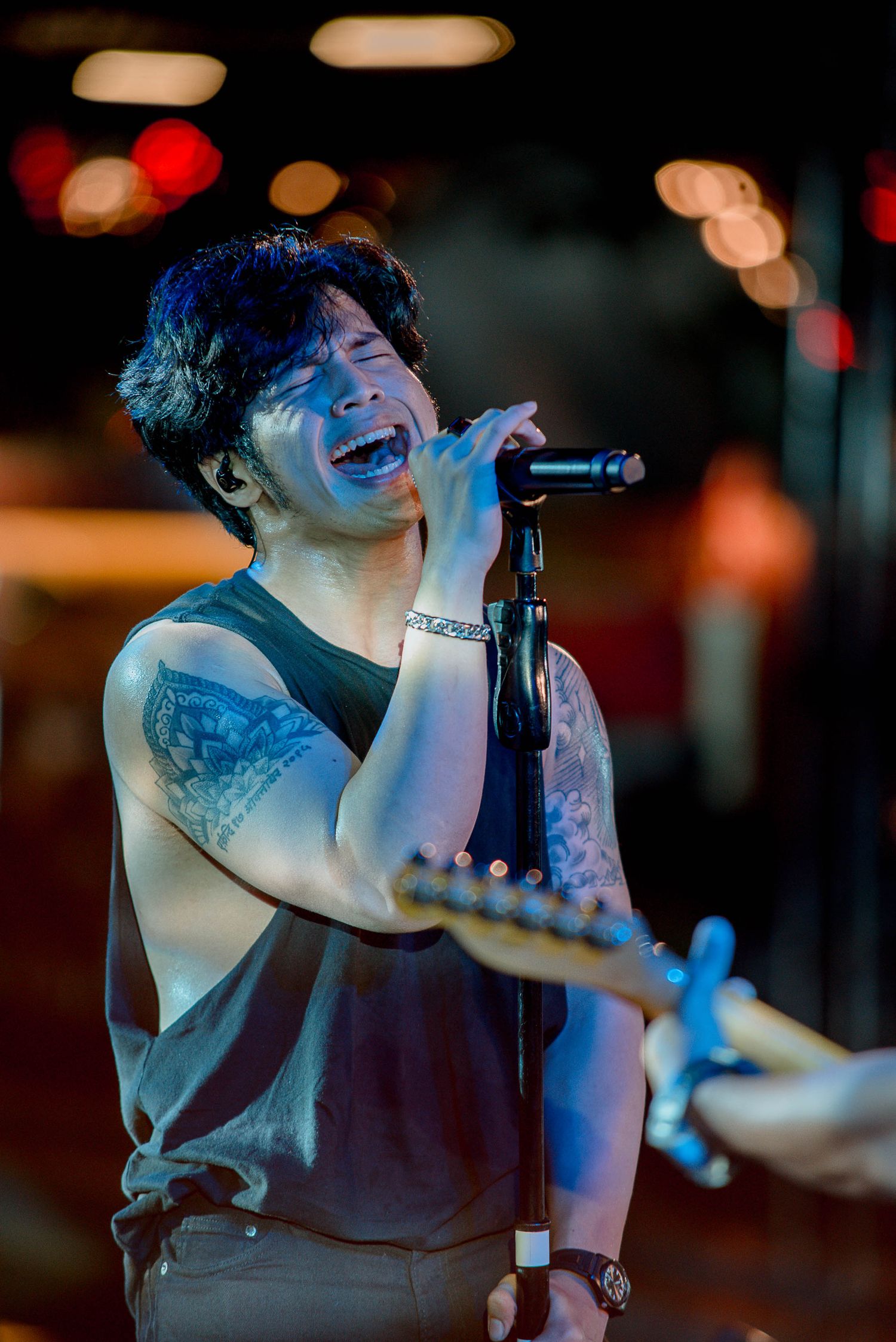 Performer sings passionately into microphone during live concert with colorful bokeh lighting.