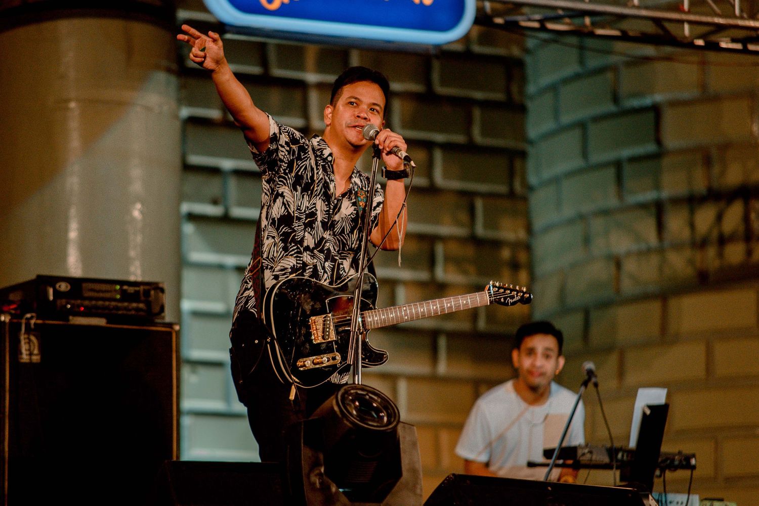 Musician in patterned shirt performing with guitar on stage.