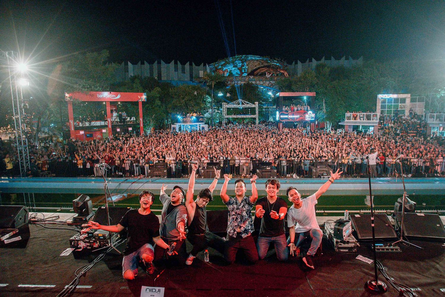 Band members pose together with large crowd of concert attendees visible in background.