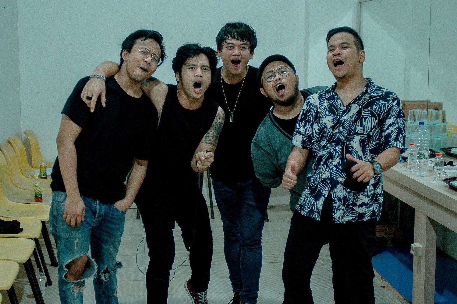 Group of musicians posing together backstage in casual attire.