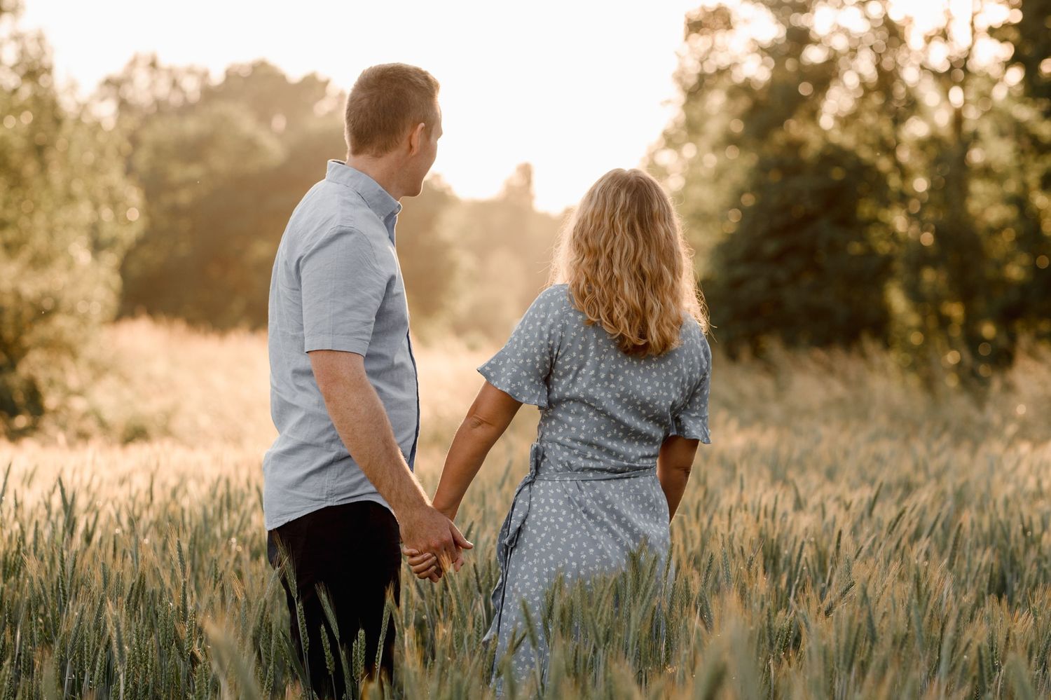 A romantic couple walks together in a golden wheat field at sunset.