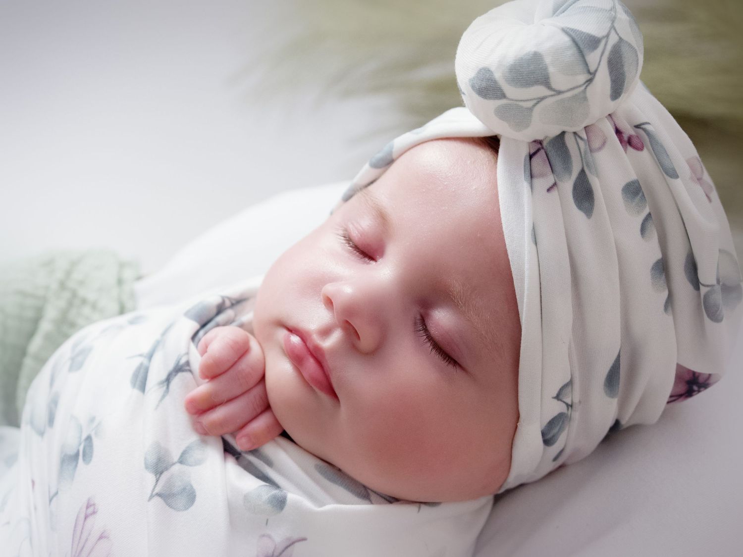 three month old baby girl laying in a basket wearing white and green floral turban wrapped