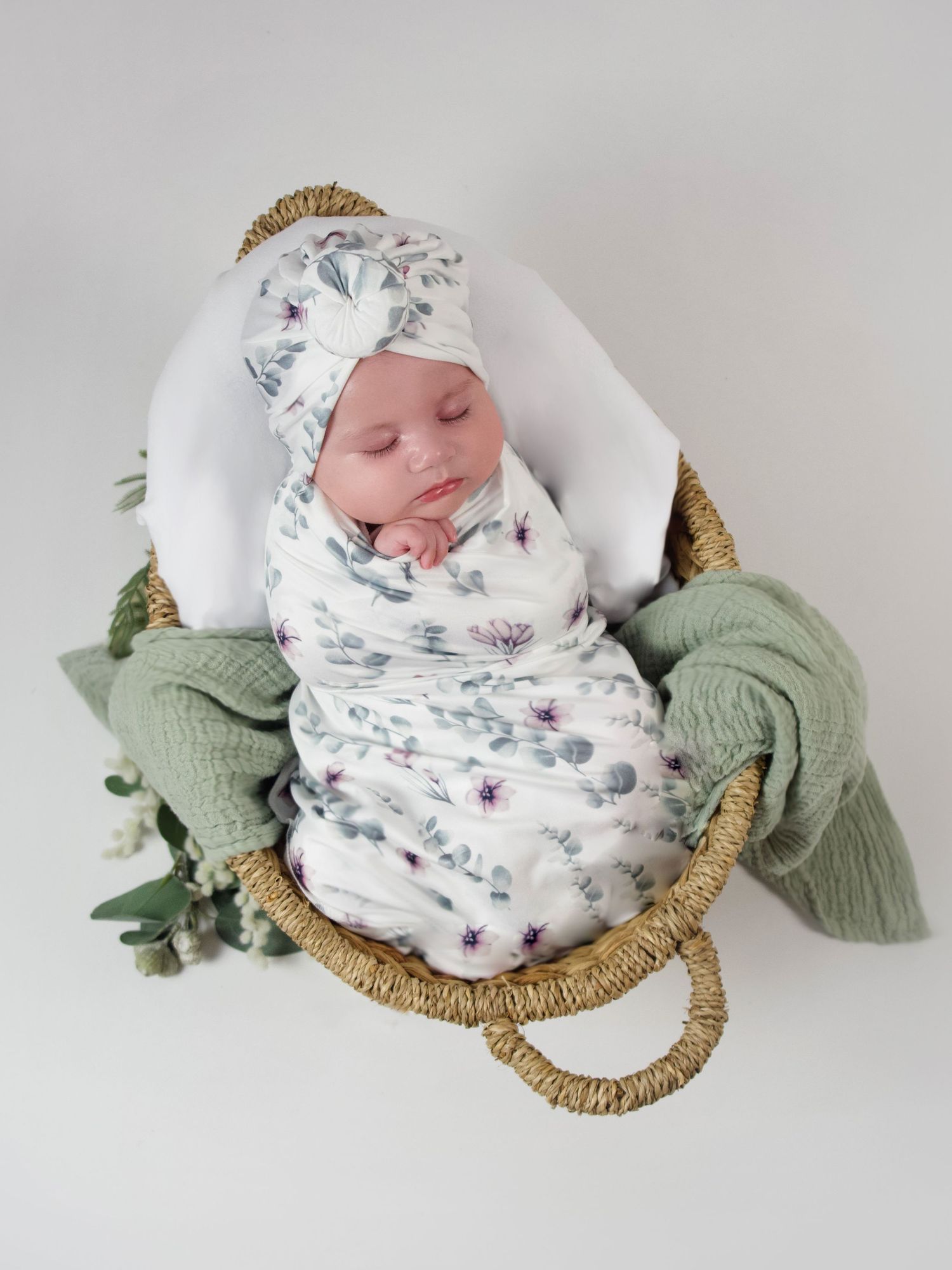 three month old baby girl laying in a basket wearing white and green floral turban wrapped