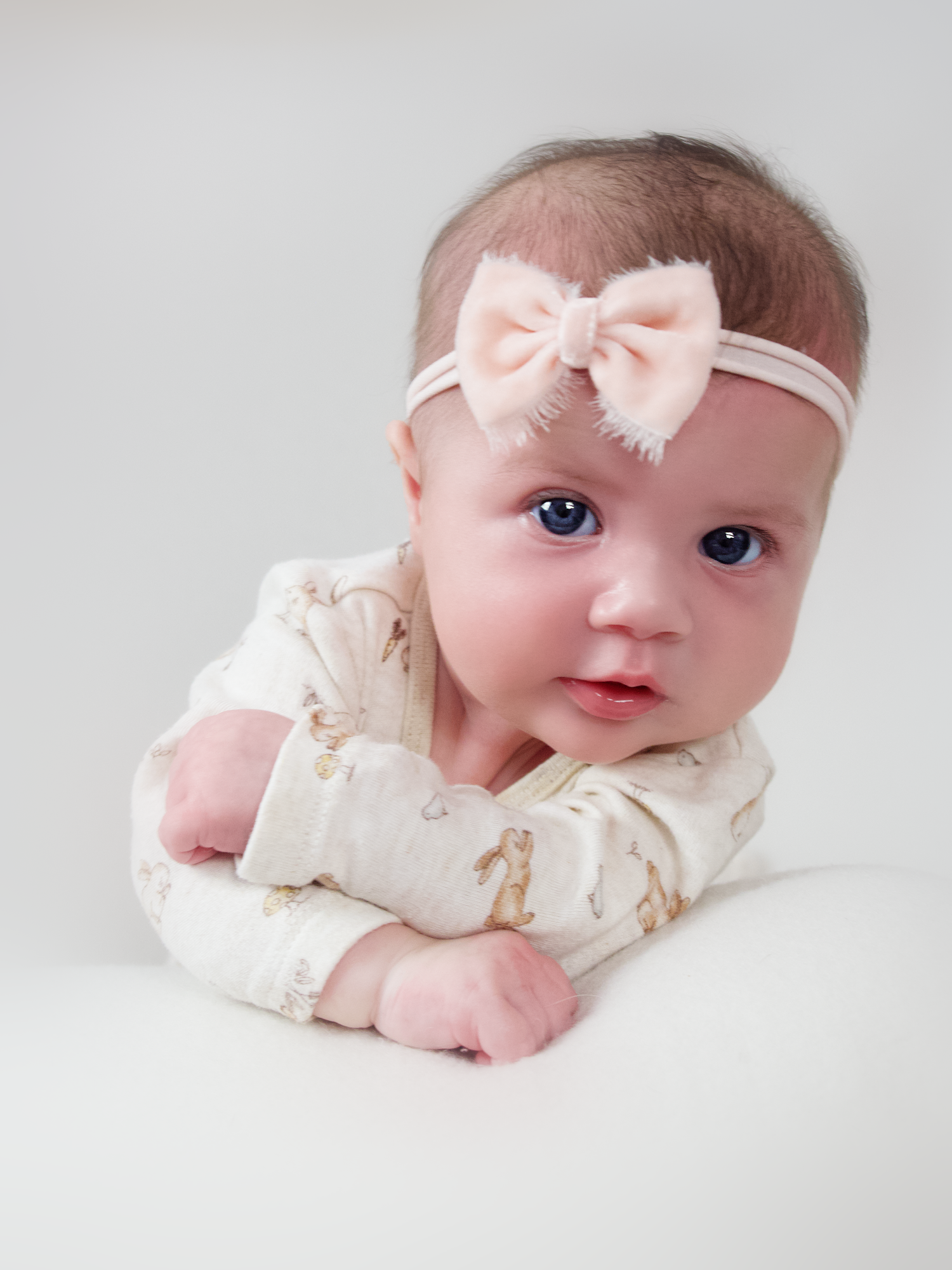 three month old baby girl laying on her stomach holding her head up wearing a pink headband looking at the camera