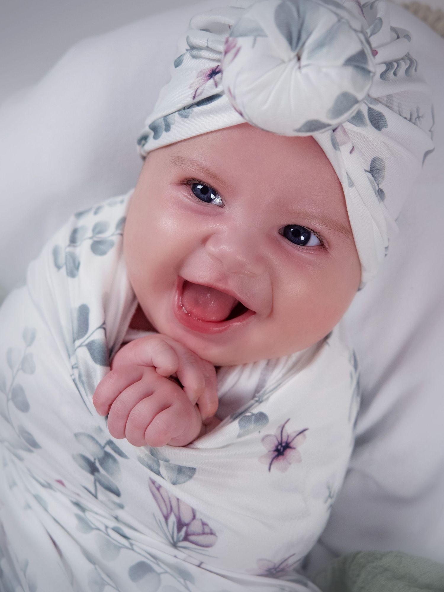 three month old baby girl laying in a basket wearing white and green floral turban wrapped