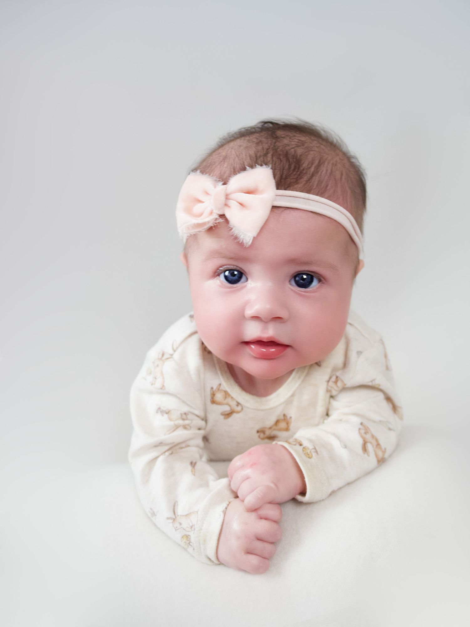 three month old baby girl laying on her stomach holding her head up wearing a pink headband looking at the camera