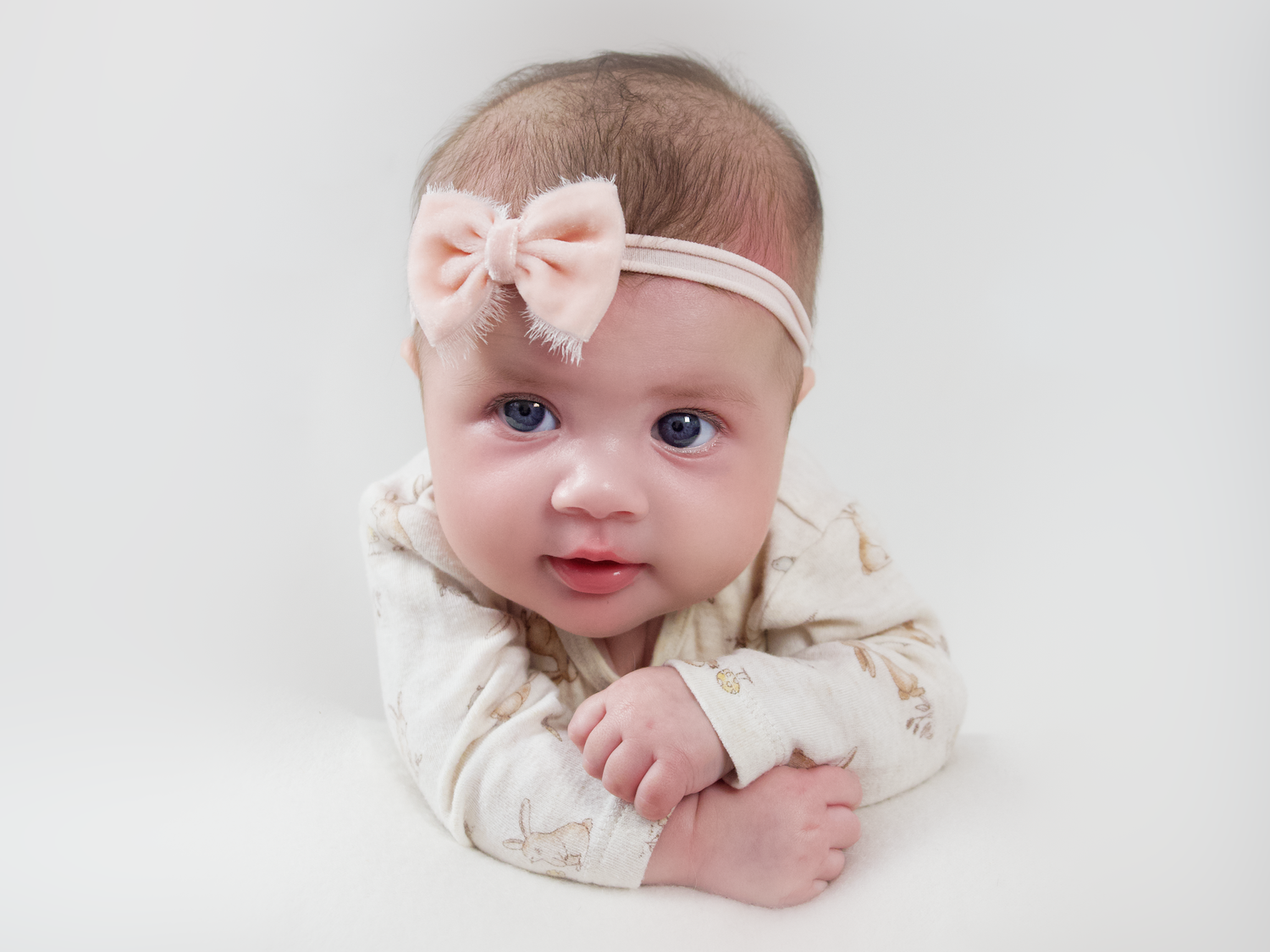 three month old baby girl laying on her stomach holding her head up wearing a pink headband looking at the camera