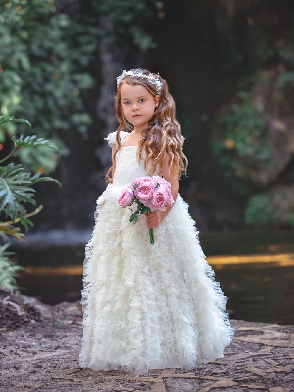 Girl in a white gown, holding a bouquet of flowers, standing in front of a waterfall for a Dream Dress Session.