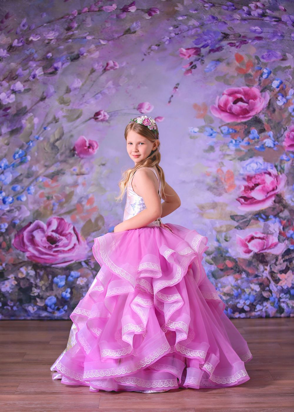Girl wearing satin couture gown looking over shoulder in front of floral studio backdrop for a Dream Dress Session.