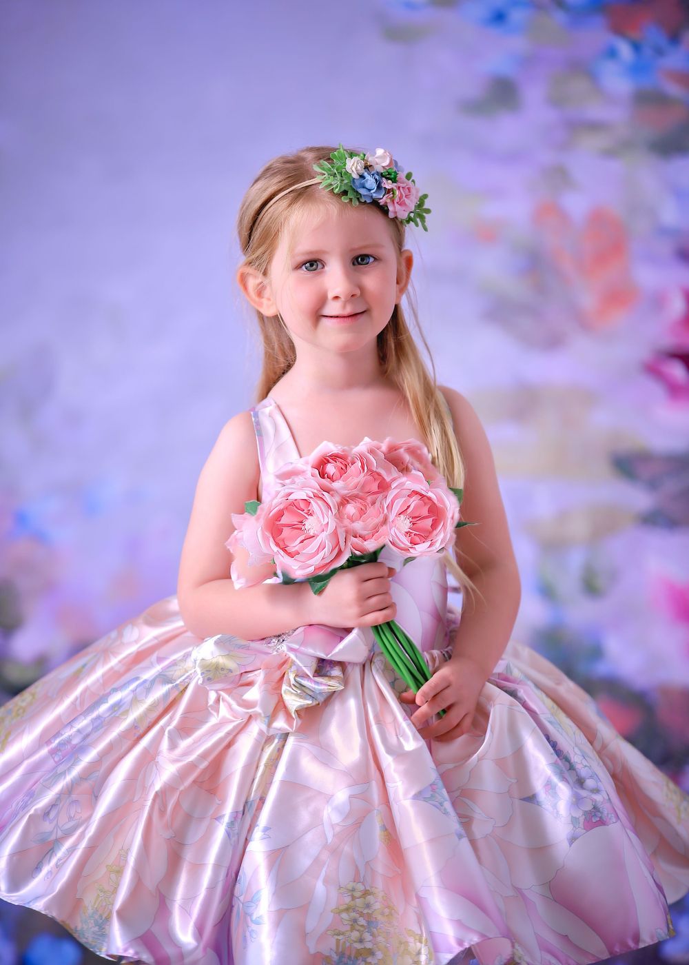 Little girl in short Satin Couture Gown holding flowers in front of floral studio backdrop for a Dream Dress Session.