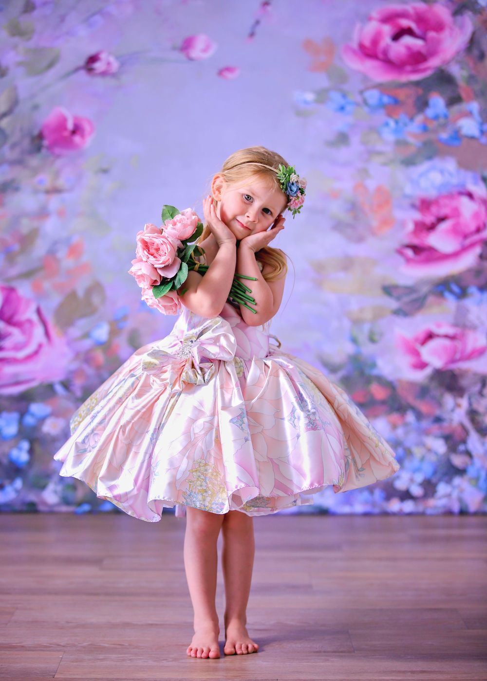Little girl in short Satin Couture Gown doing a cute pose in front of floral studio backdrop for a Dream Dress Session.
