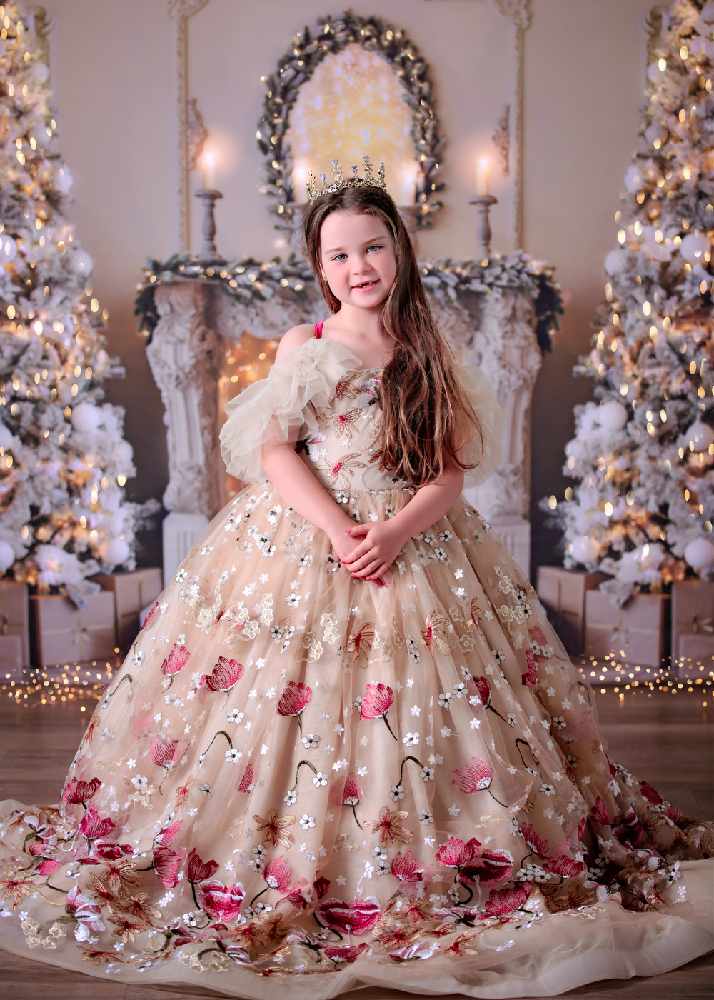 Girl wearing a crown and gold and red embroidered gown standing in front of sparkly golden style Christmas backdrop.