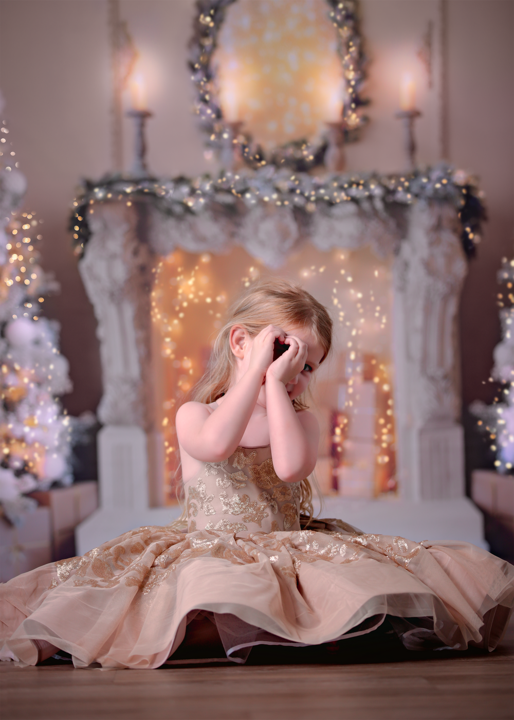 Girl sitting on floor in front of Christmas themed studio backdrop, peeking through a love heart made with her hands.