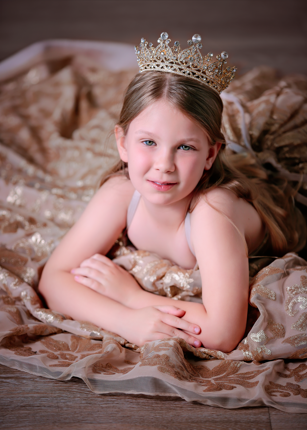 Girl wearing a crown and gold sequin dress laying on her front propped up on her elbows for a Dream Dress Session