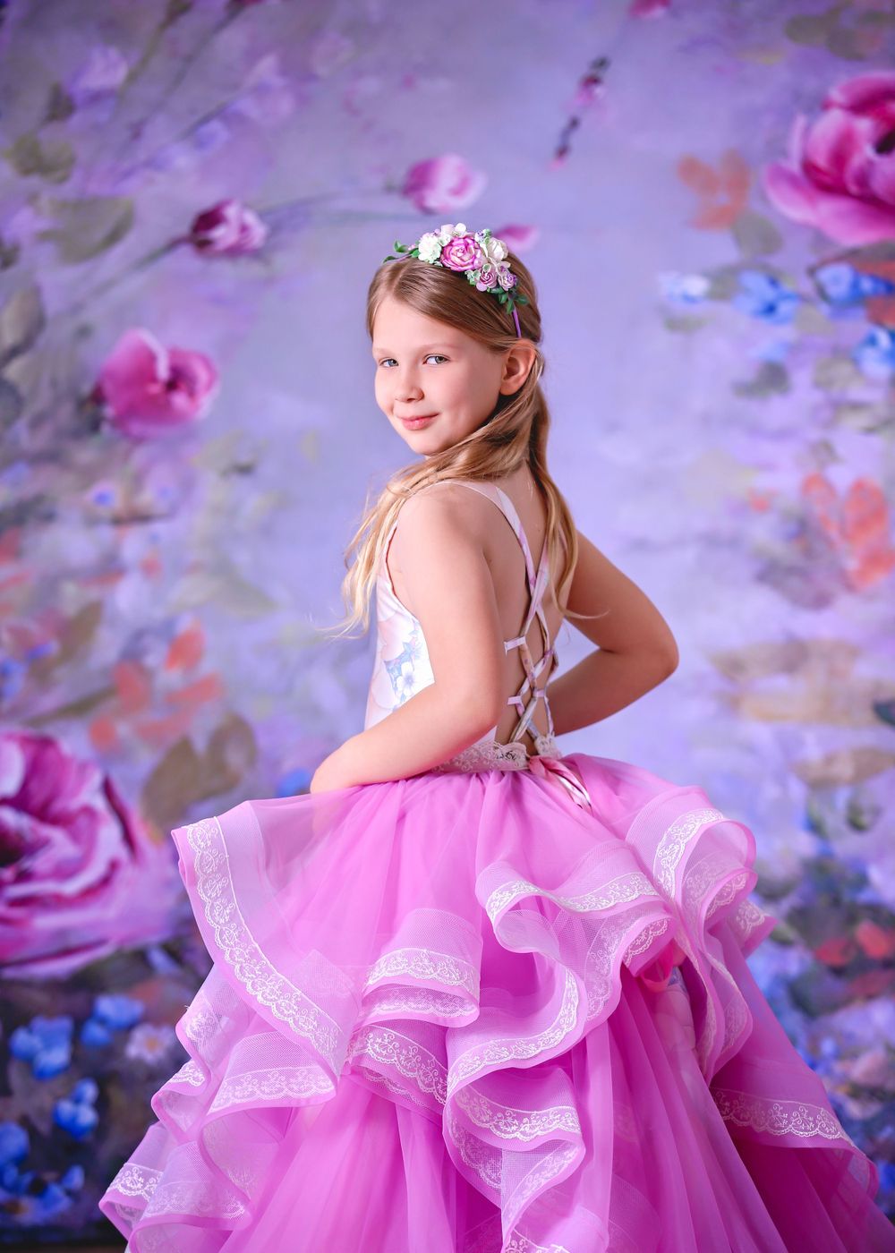 Girl wearing satin couture gown looking over shoulder in front of floral studio backdrop for a Dream Dress Session.