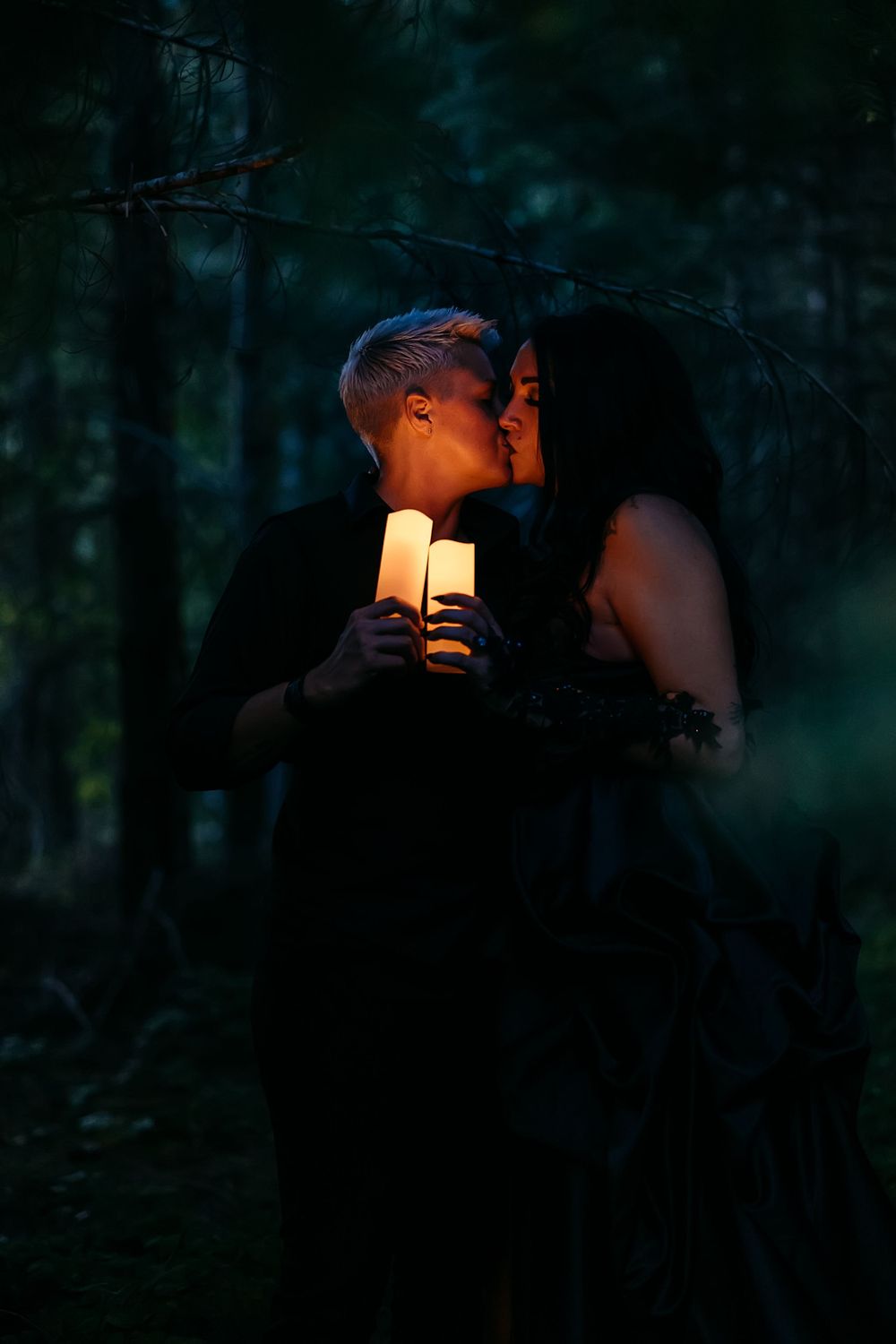 A romantic candlelit moment in a dark forest with a couple in formal black attire.