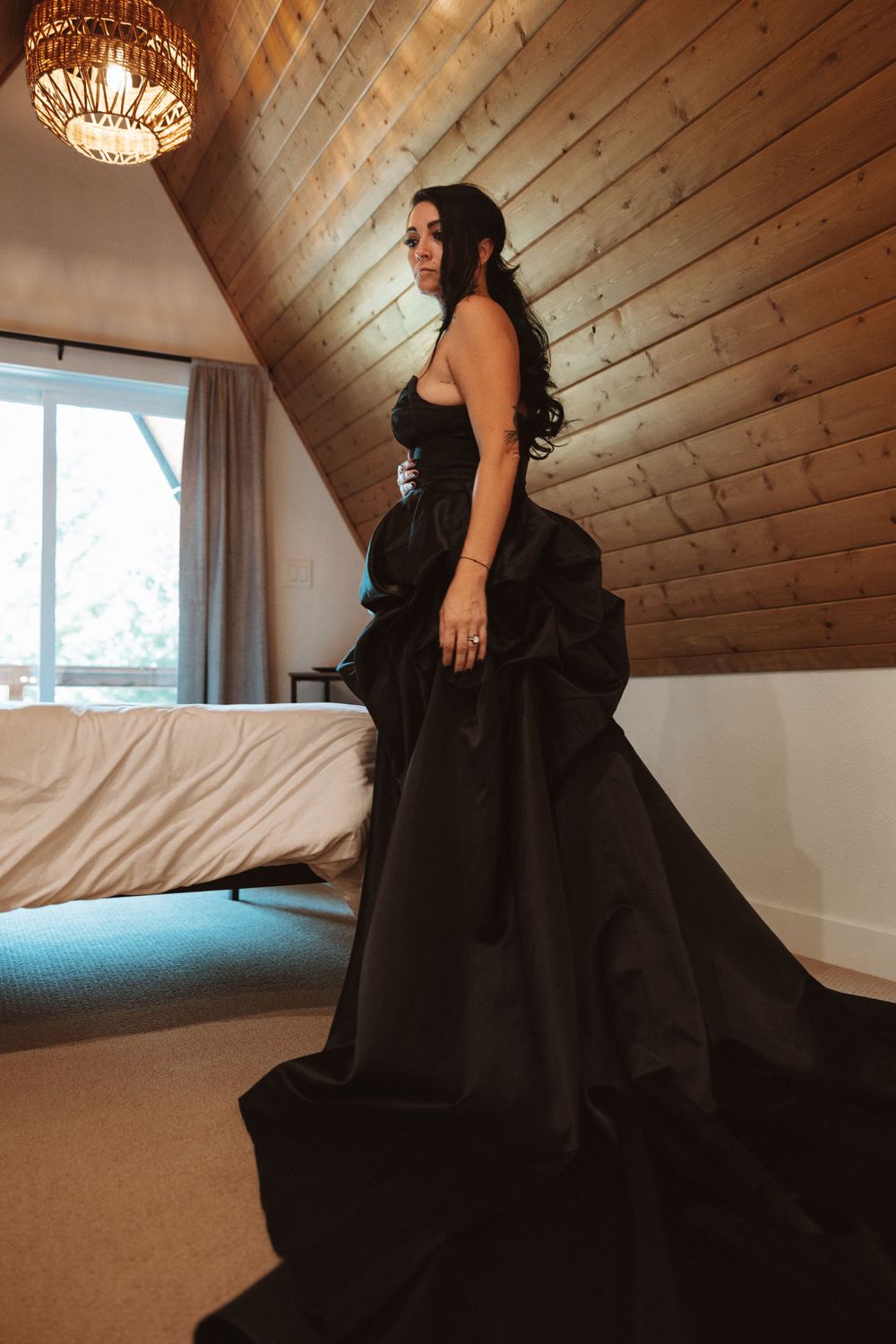Person wearing an elegant black ballgown in a rustic wooden room with a chandelier.