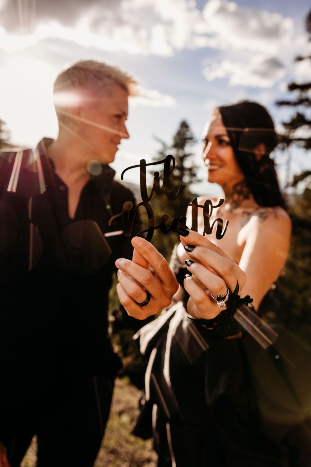 A couple toasts with wine glasses in sunlit forest scenery.