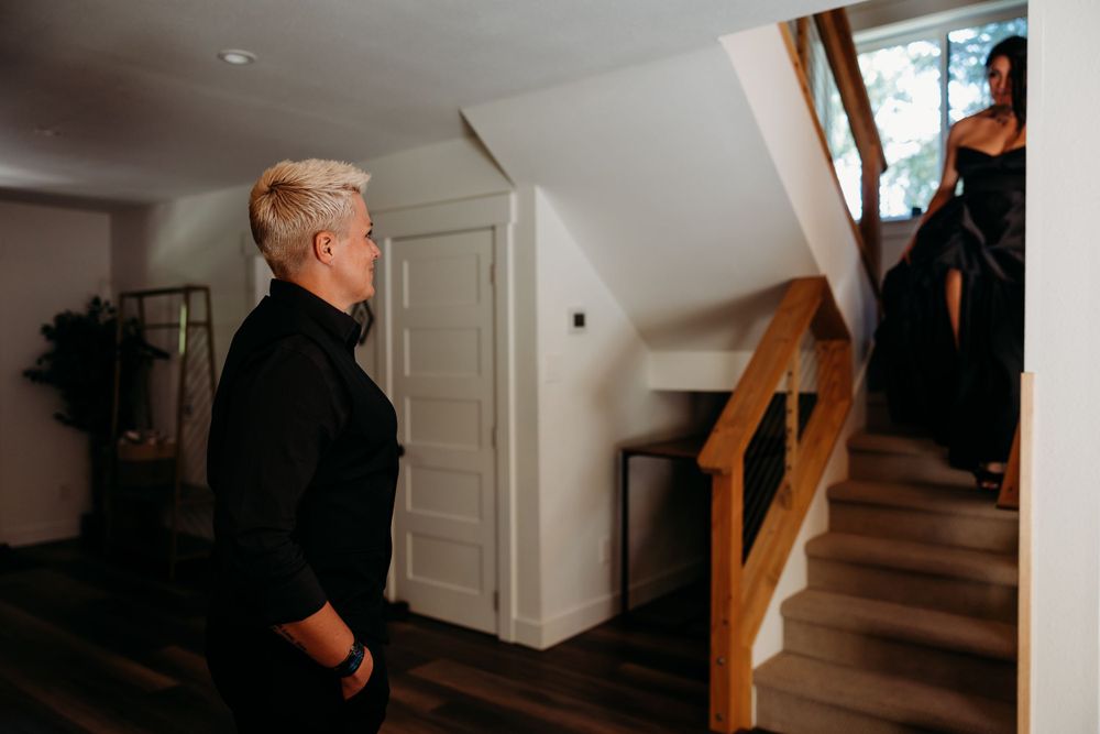 Person in black clothing standing at the bottom of wooden stairs in a home.