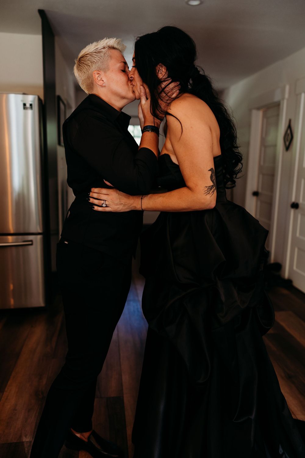 Couple sharing an intimate moment in a black dress and suit in their home.