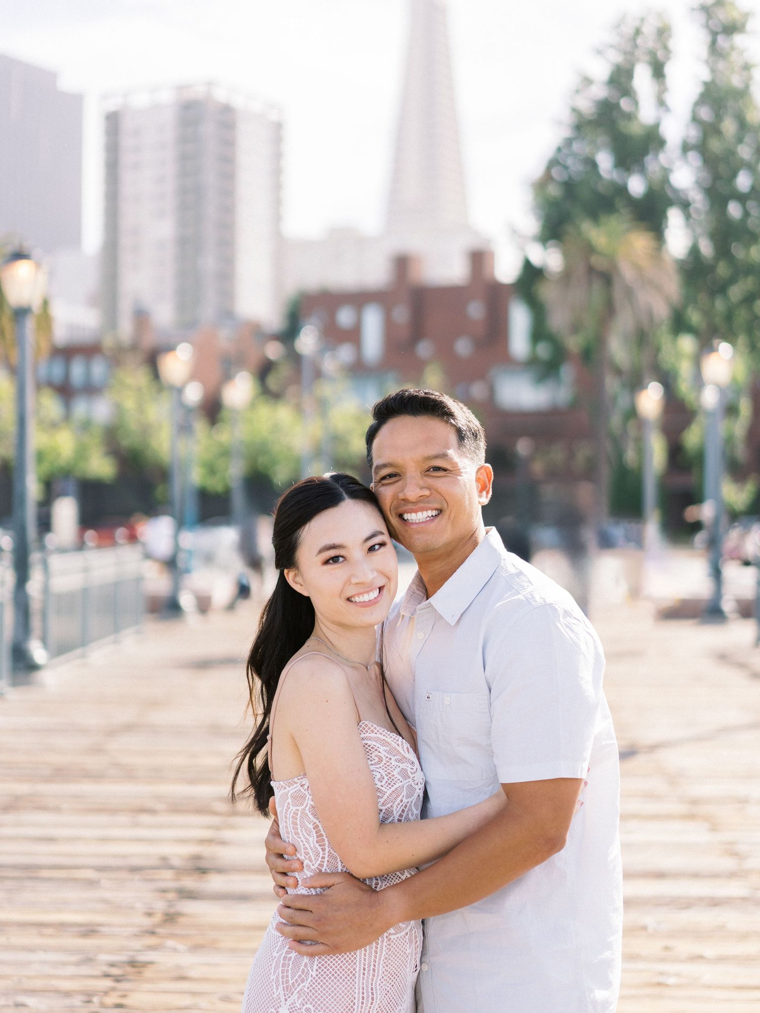 A happy couple poses on a pier with the San Francisco skyline behind them.