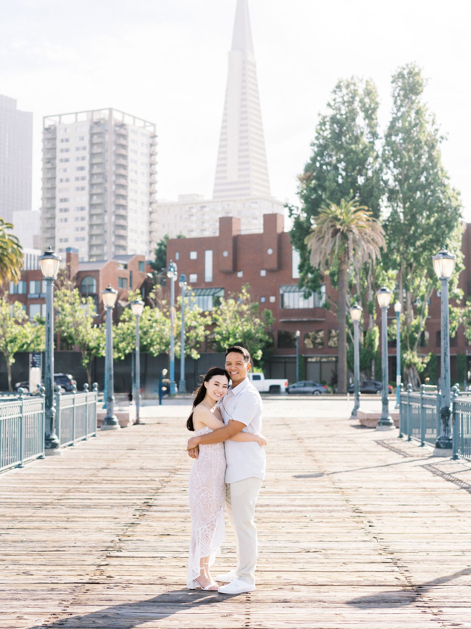 A couple embraces on a pier with the San Francisco Transamerica Pyramid in the background.