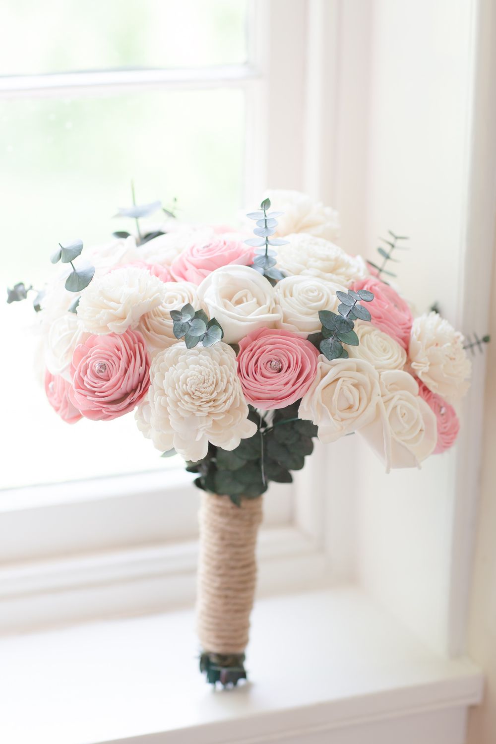 Pink and white rose wedding bouquet wrapped in twine sits on windowsill in natural light.
