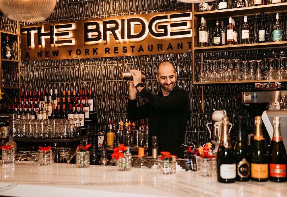 Bartenders working behind counter at The Bridge Restaurant with illuminated signage.