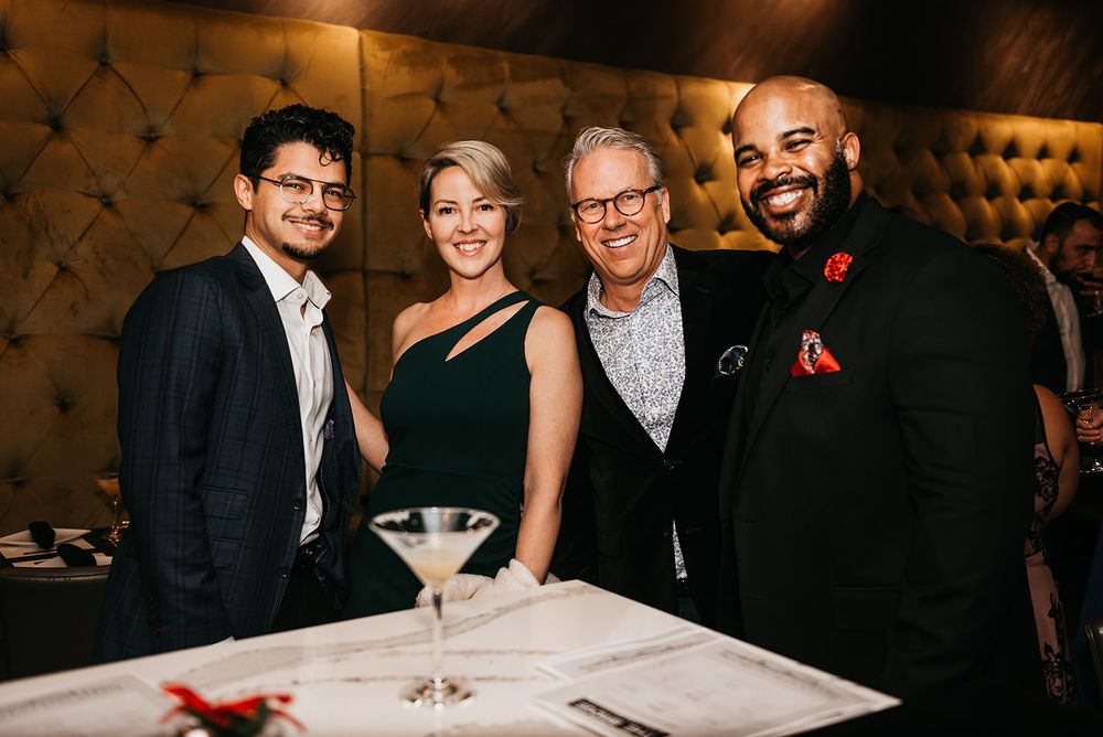 Group of well-dressed guests posing with martini glass at formal event.