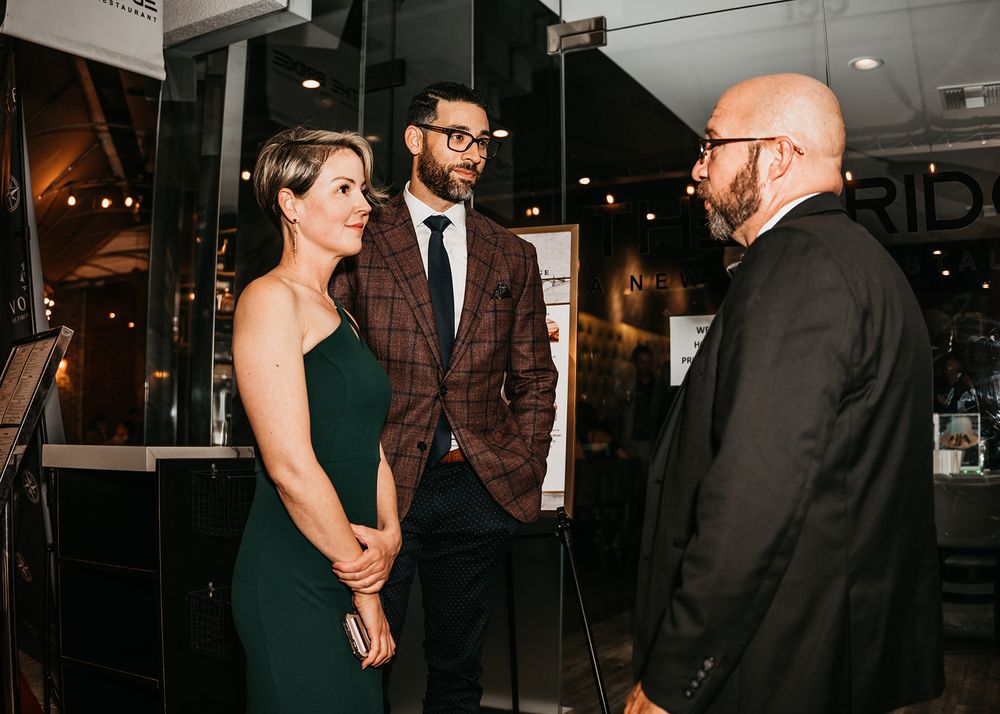 Three people having conversation in formal attire at upscale venue entrance.