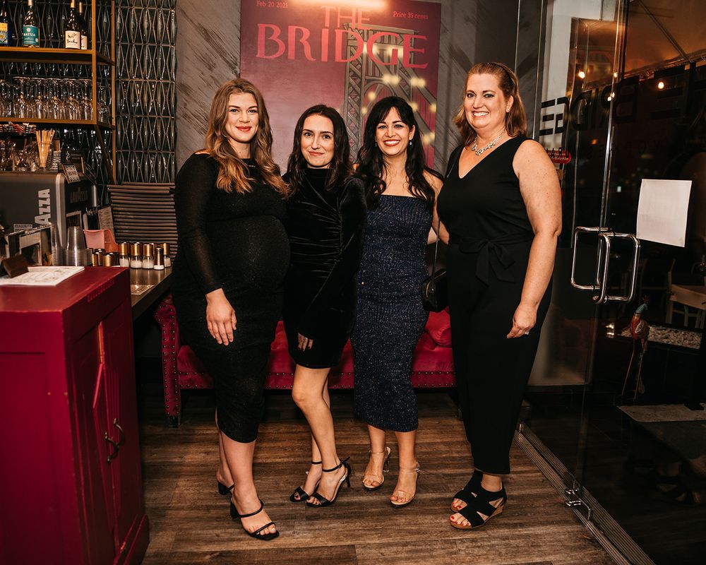 Four women in black dresses pose at elegant event venue with red decor.