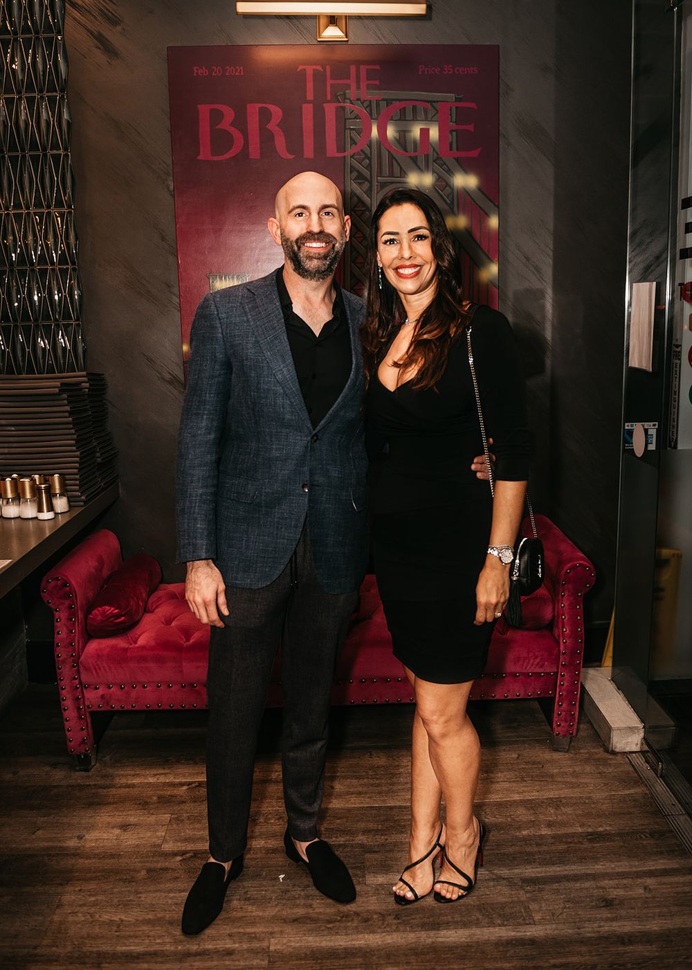 Couple poses in front of red illuminated sign at upscale venue.