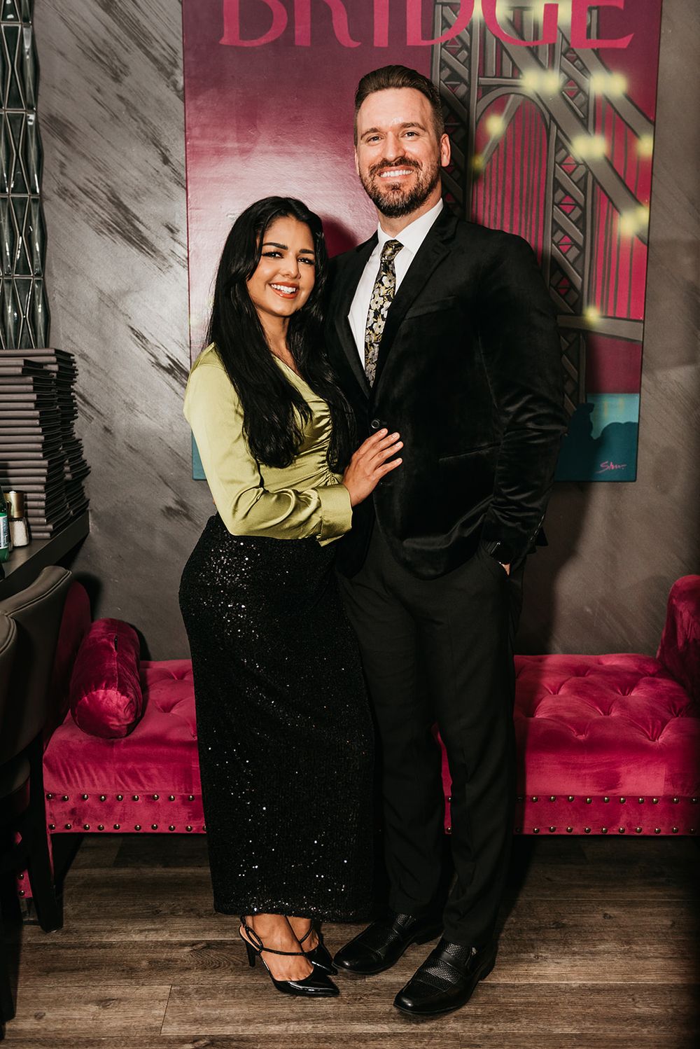 A couple poses in formal attire against a pink backdrop at The Bridge event.