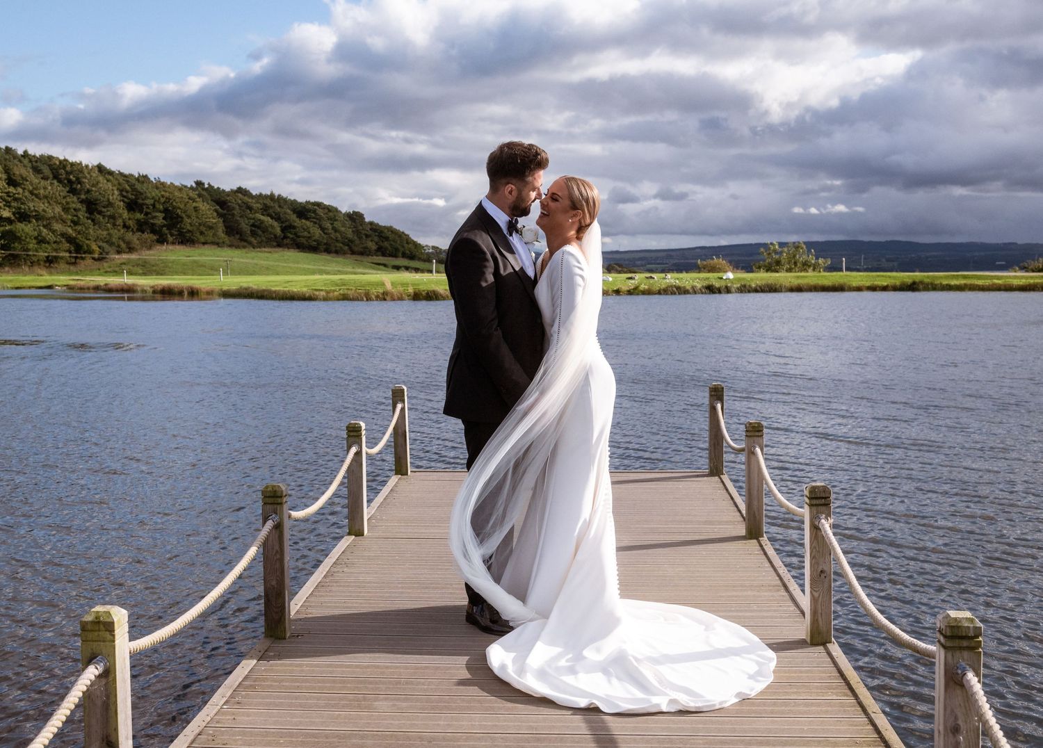 A romantic wedding portrait on a wooden pier overlooking a serene lake and mountains at the Vu Bathgate