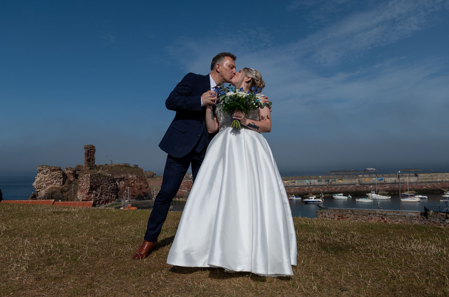 Newlyweds share romantic moment on coastal clifftop with ocean view.
