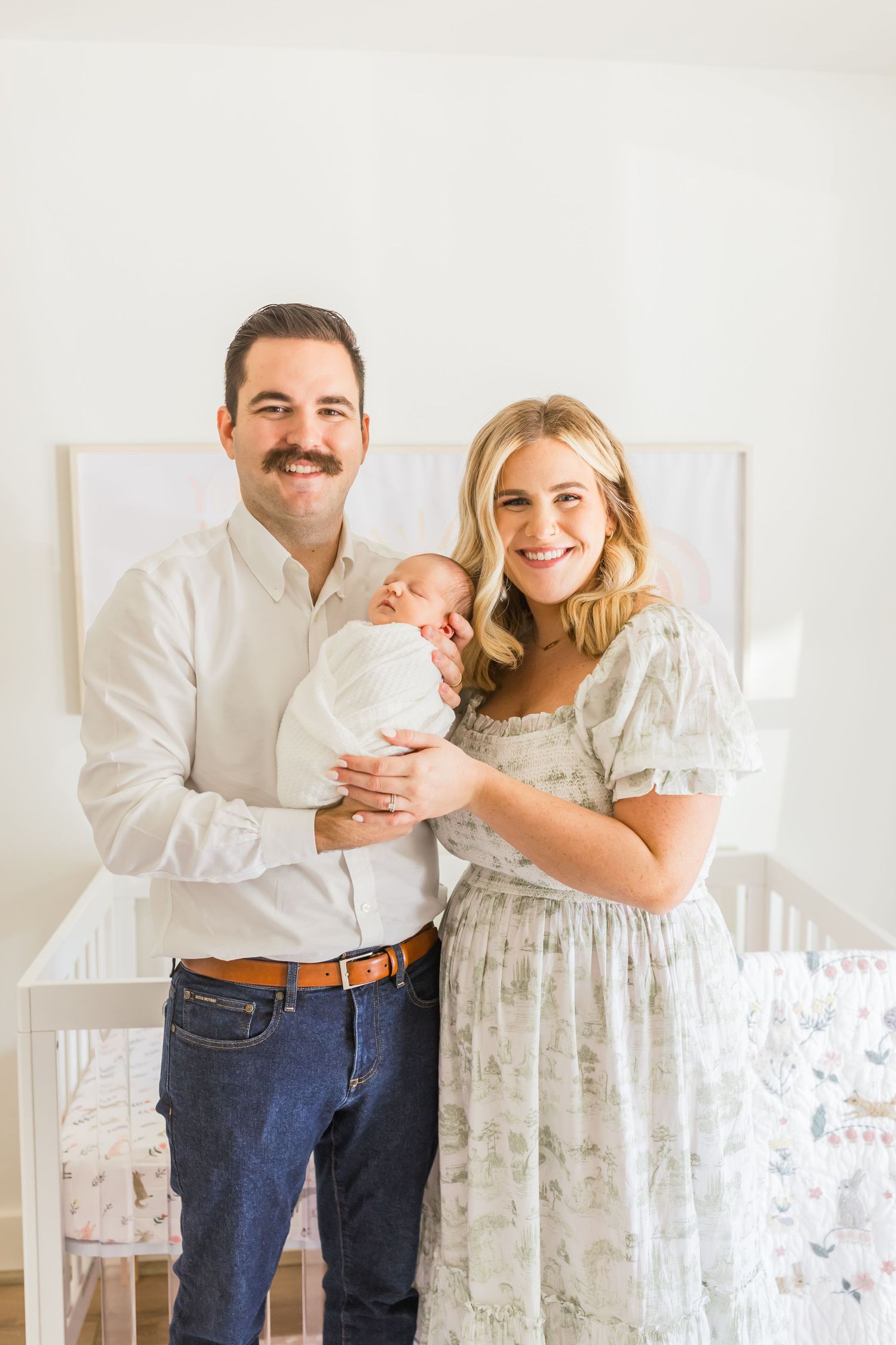 A family portrait in front of white crib and pastel wall art in modern nursery.