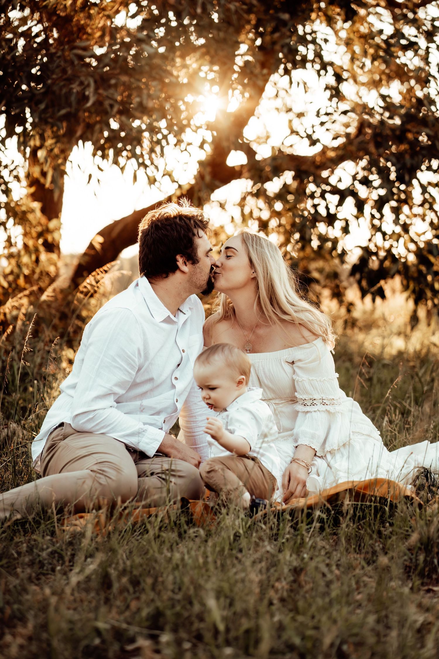Family in white clothing sitting together on grass during golden hour sunset.