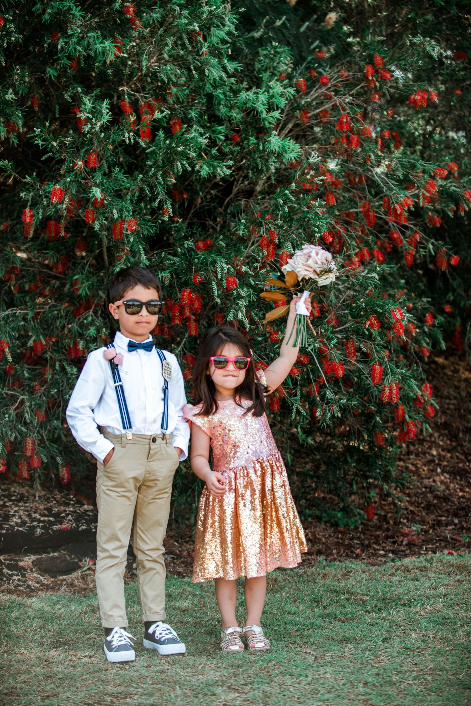 Two young attendants in formal wear pose against flowering bush.
