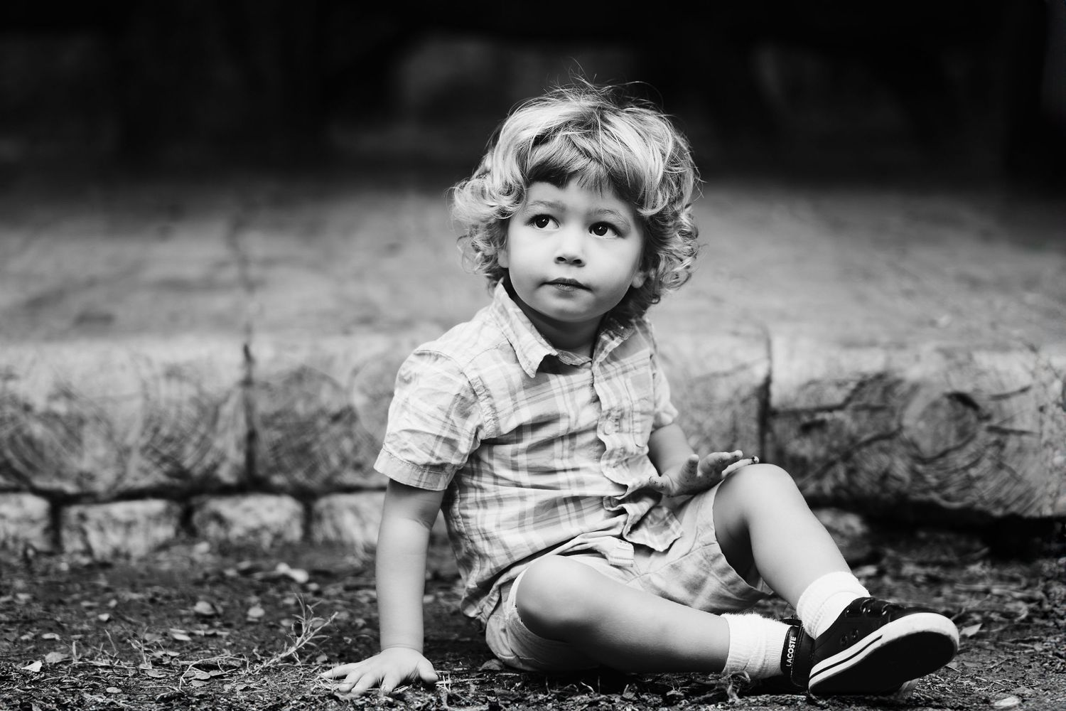 a black and white portrait of a toddler boy with curly hair sitting on the ground at Landa Gardens at Landa Library