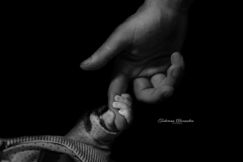 Black and white close-up of adult hand holding tiny baby hand.