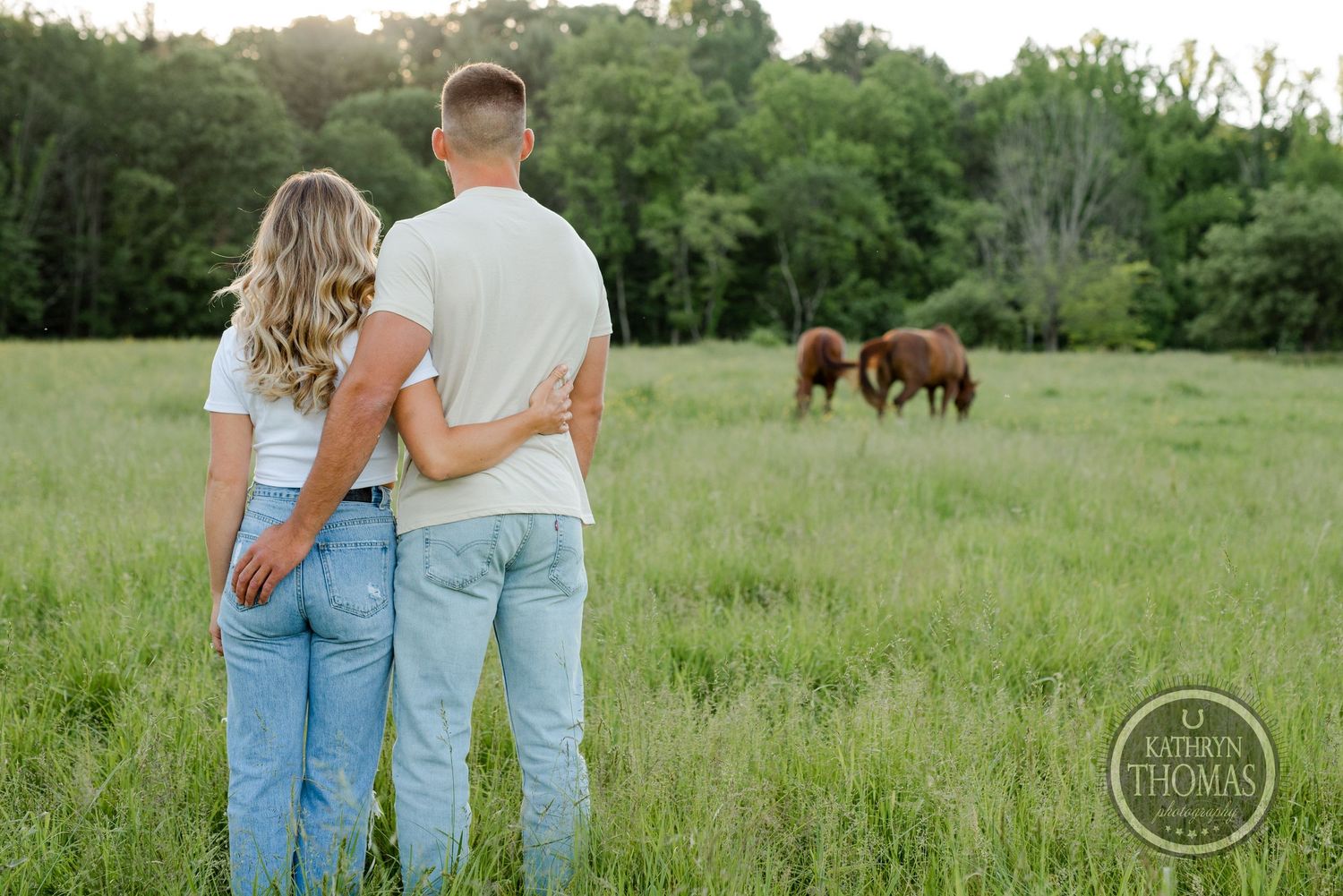 Couple stands together watching horses graze in peaceful meadow.